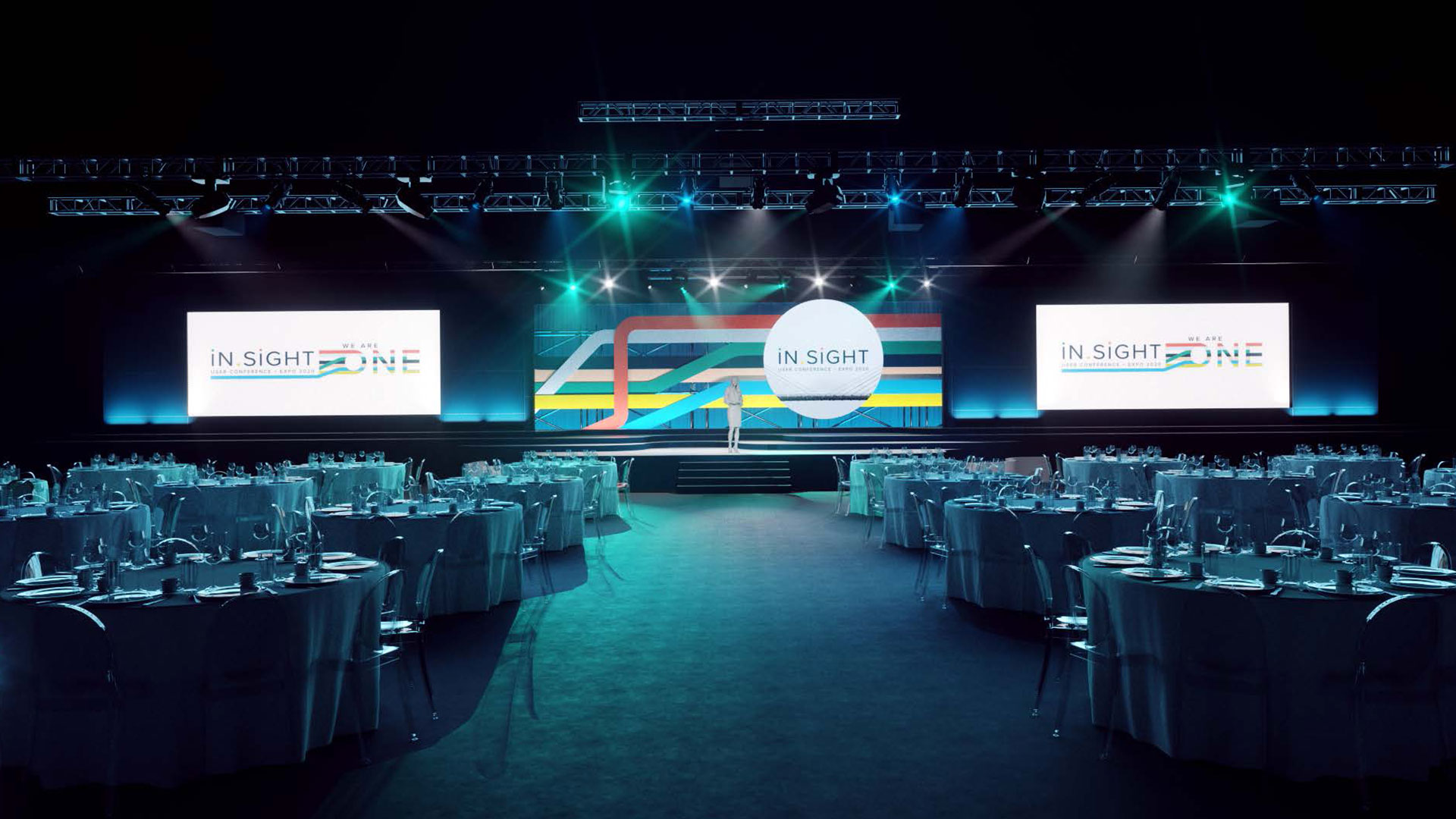 A large conference or gala event setup featuring a stage with two large screens displaying 'In Sight One' branding. The room is elegantly arranged with round tables covered in white tablecloths and set with silverware and glassware. Blue and green lighting illuminates the stage and the room, creating a sophisticated and professional atmosphere. Truss structures with additional lighting are positioned above the stage.