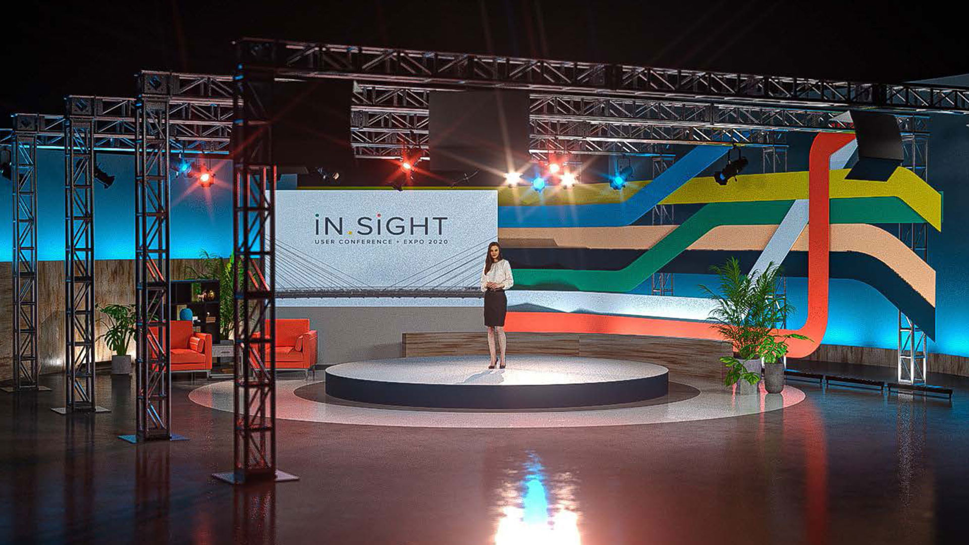 A modern studio setup designed for a virtual conference, featuring a presenter standing on a circular stage with a large screen behind displaying the 'In Sight User Conference + Expo 2020' branding. The studio includes truss structures with lighting, colorful wall graphics, potted plants, and red chairs, creating a vibrant and professional environment for virtual events.